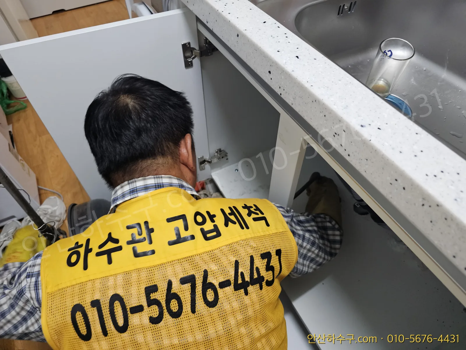 노란 조끼 작업자가 싱크대 하부장의 수전·배관을 점검하는 모습